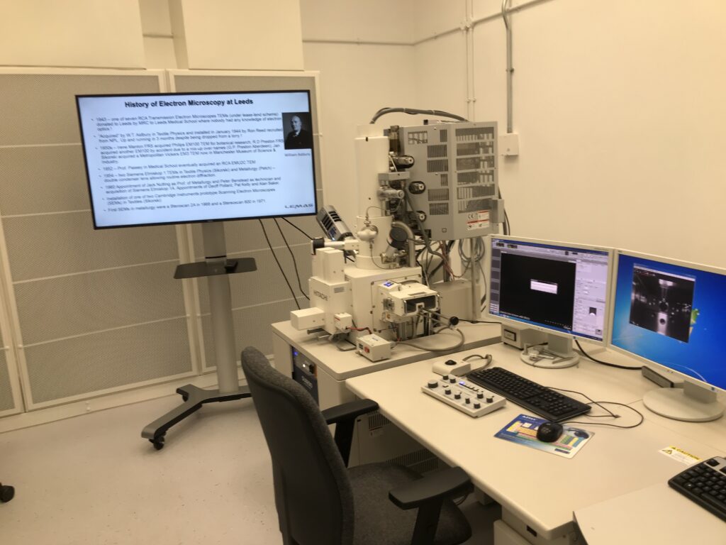 Powerful electron microscopes at LEMAS centre, University of Leeds with slide detailing history of electron microscopy at Leeds in the background